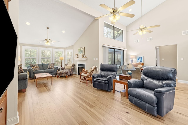 living room featuring light wood-type flooring, visible vents, a lit fireplace, and a ceiling fan