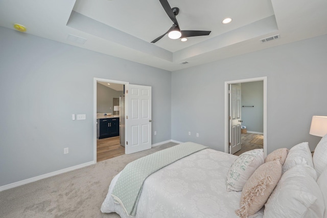 bedroom featuring visible vents, light colored carpet, baseboards, and a tray ceiling