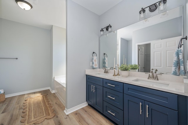 bathroom with double vanity, a garden tub, wood finished floors, and a sink