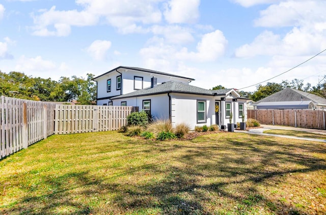 rear view of house featuring stucco siding, a yard, and a fenced backyard