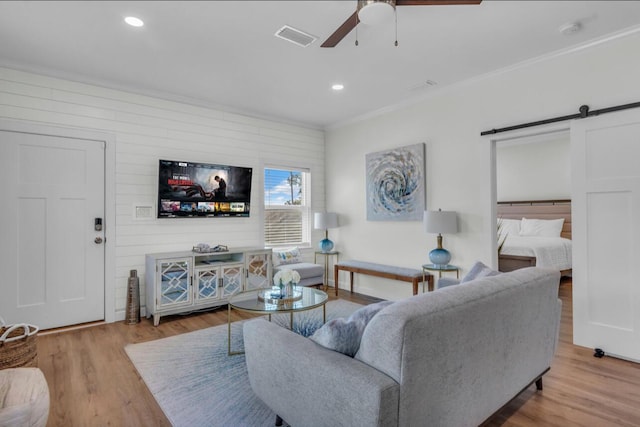 living room featuring visible vents, a barn door, ornamental molding, recessed lighting, and wood finished floors