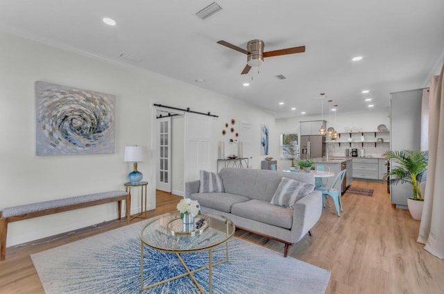 living area featuring a ceiling fan, light wood finished floors, recessed lighting, crown molding, and a barn door