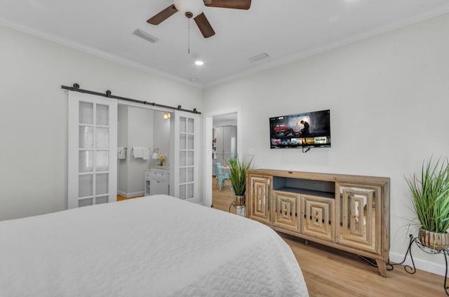 bedroom featuring visible vents, a barn door, crown molding, light wood finished floors, and baseboards