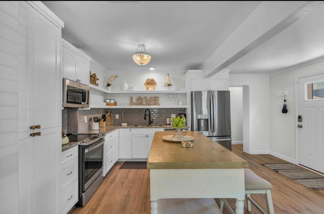 kitchen featuring open shelves, light stone counters, a sink, stainless steel appliances, and decorative backsplash