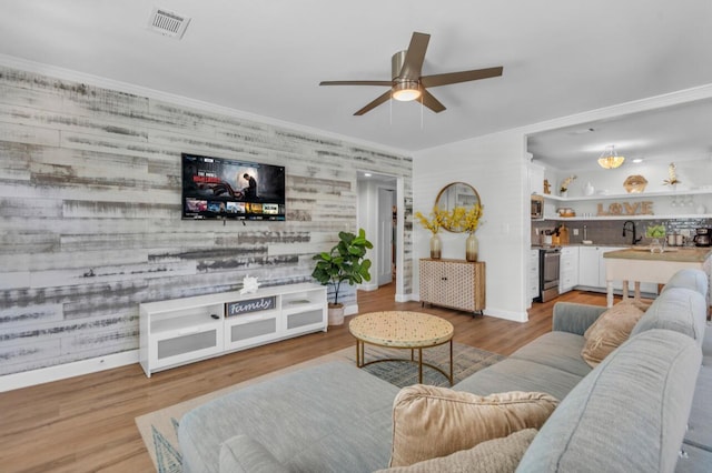 living area featuring visible vents, crown molding, ceiling fan, baseboards, and wood finished floors