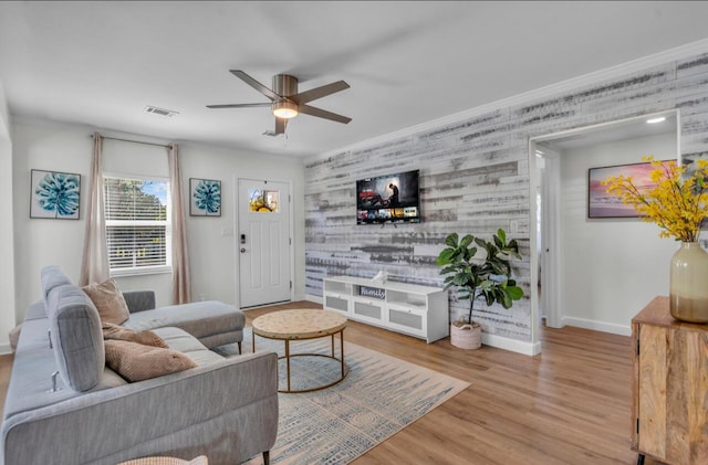 living room with a ceiling fan, wood finished floors, visible vents, baseboards, and an accent wall