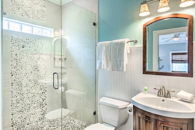 bathroom with ceiling fan, toilet, wainscoting, a stall shower, and vanity