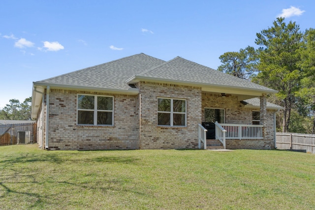 back of house featuring a ceiling fan, fence, a shingled roof, a lawn, and brick siding