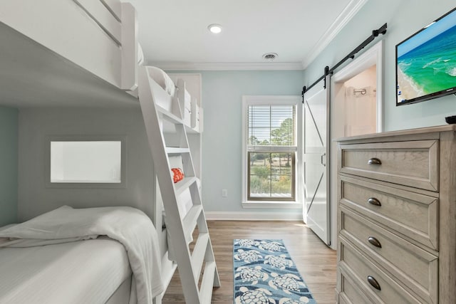 bedroom with visible vents, light wood-style flooring, a barn door, crown molding, and baseboards