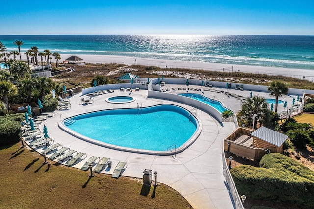 community pool with a view of the beach, a patio area, a water view, and a hot tub