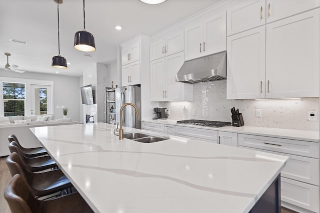 kitchen with a sink, under cabinet range hood, stainless steel appliances, white cabinetry, and a kitchen island with sink