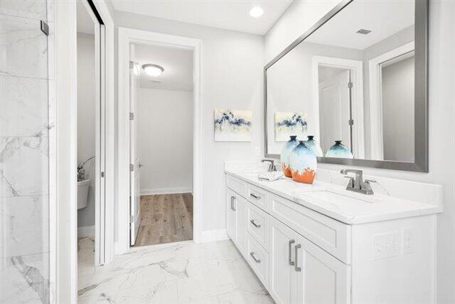 full bathroom with marble finish floor, a sink, a marble finish shower, double vanity, and baseboards