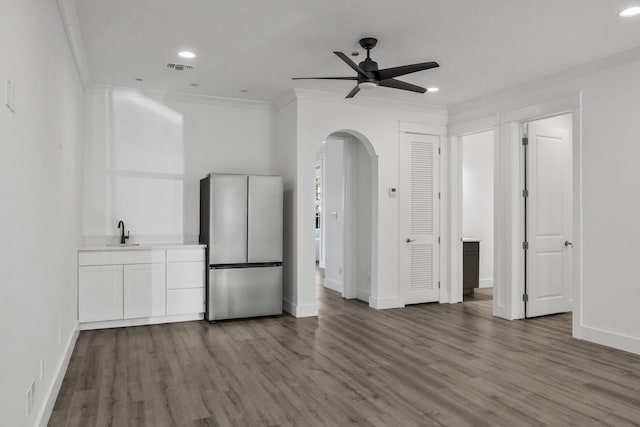 unfurnished living room featuring ceiling fan, ornamental molding, dark wood-style floors, arched walkways, and a sink