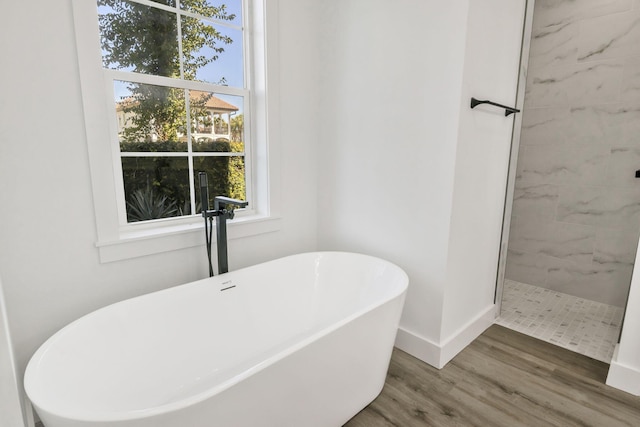 bathroom with a soaking tub, tiled shower, baseboards, and wood finished floors