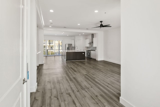 unfurnished living room featuring a ceiling fan, wood finished floors, baseboards, recessed lighting, and a sink