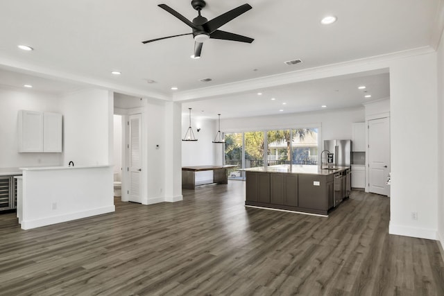 kitchen with dark wood-type flooring, open floor plan, an island with sink, ornamental molding, and a ceiling fan