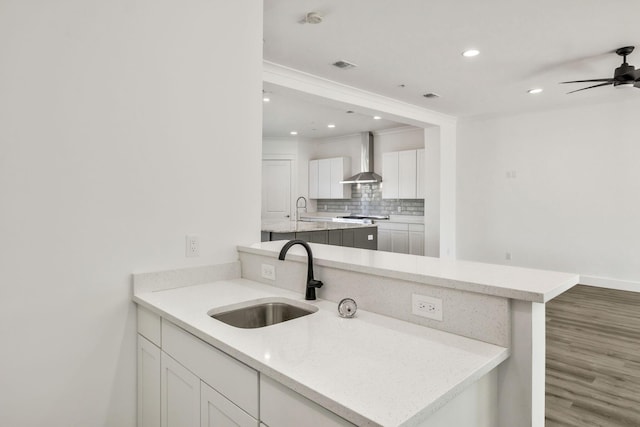 kitchen with wood finished floors, visible vents, a sink, wall chimney range hood, and tasteful backsplash