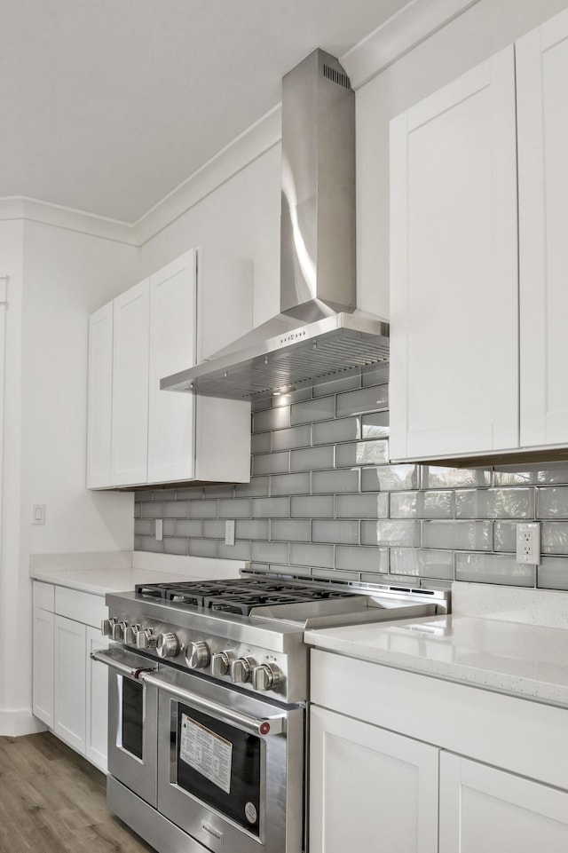 kitchen with tasteful backsplash, white cabinetry, wall chimney exhaust hood, and range with two ovens