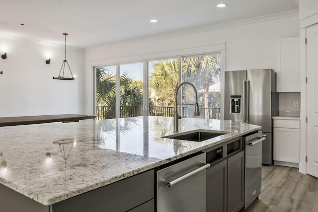 kitchen with light stone counters, a sink, light wood-style floors, appliances with stainless steel finishes, and crown molding