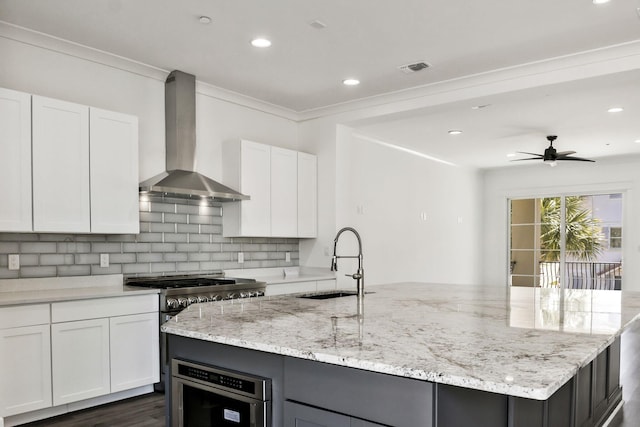 kitchen with tasteful backsplash, high end stainless steel range, an island with sink, wall chimney exhaust hood, and a sink