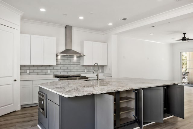 kitchen with visible vents, an island with sink, a sink, backsplash, and wall chimney exhaust hood