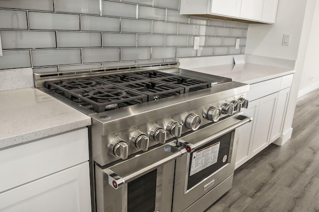 kitchen with light stone countertops, wood finished floors, range with two ovens, decorative backsplash, and white cabinetry