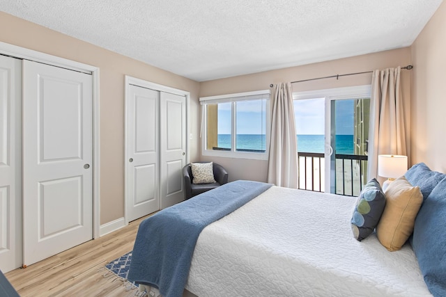 bedroom with a water view, light wood-style flooring, a textured ceiling, baseboards, and access to exterior