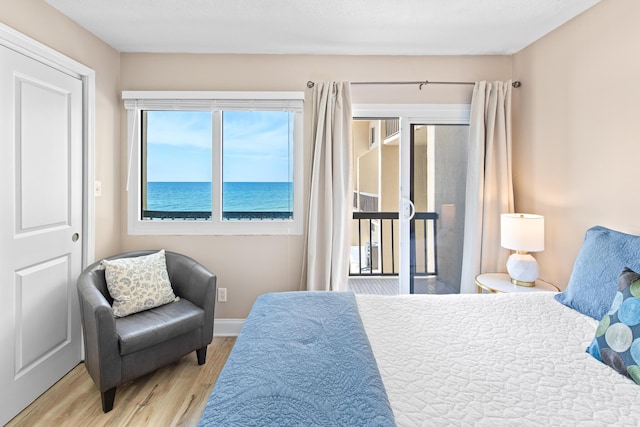 bedroom with baseboards, wood finished floors, and access to exterior