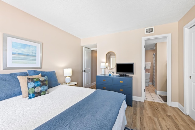 bedroom with visible vents, ensuite bath, light wood-type flooring, and baseboards