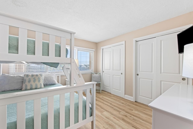 bedroom with light wood-style flooring, baseboards, multiple closets, and a textured ceiling