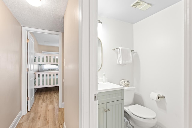 bathroom featuring visible vents, toilet, vanity, wood finished floors, and a textured ceiling