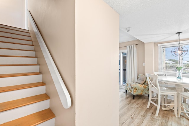 stairs featuring a textured ceiling, an inviting chandelier, and wood finished floors