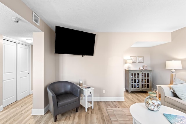 living area with visible vents, baseboards, a textured ceiling, and wood finished floors