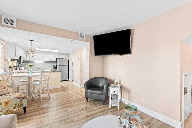 living area featuring baseboards, visible vents, and light wood finished floors