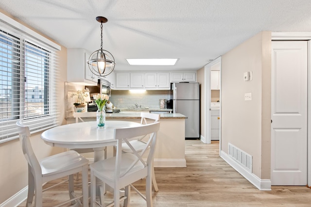 dining space with visible vents, baseboards, light wood-style floors, and a textured ceiling