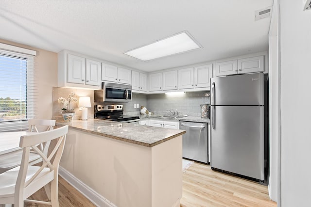 kitchen featuring decorative backsplash, appliances with stainless steel finishes, a peninsula, and a sink