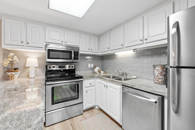 kitchen with light wood-type flooring, light stone counters, white cabinets, stainless steel appliances, and a sink