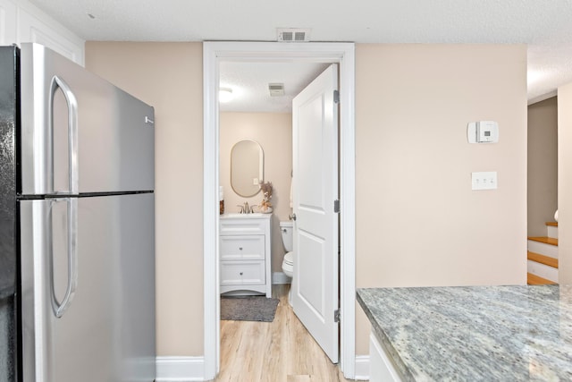 kitchen featuring light wood finished floors, visible vents, freestanding refrigerator, a textured ceiling, and a sink