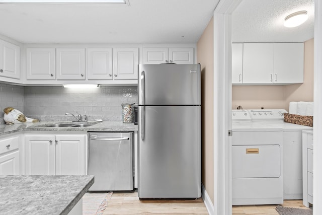 kitchen with independent washer and dryer, white cabinets, stainless steel appliances, and a sink