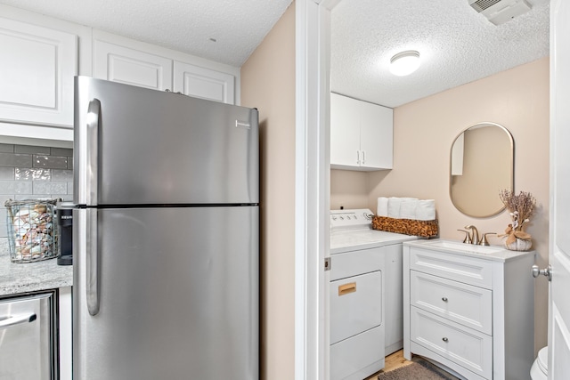 kitchen with white cabinetry, washer / clothes dryer, freestanding refrigerator, and a sink