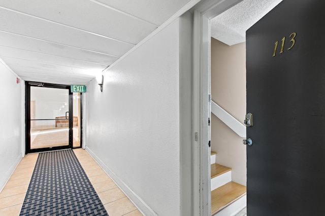 corridor with stairway, light tile patterned flooring, baseboards, and a textured ceiling