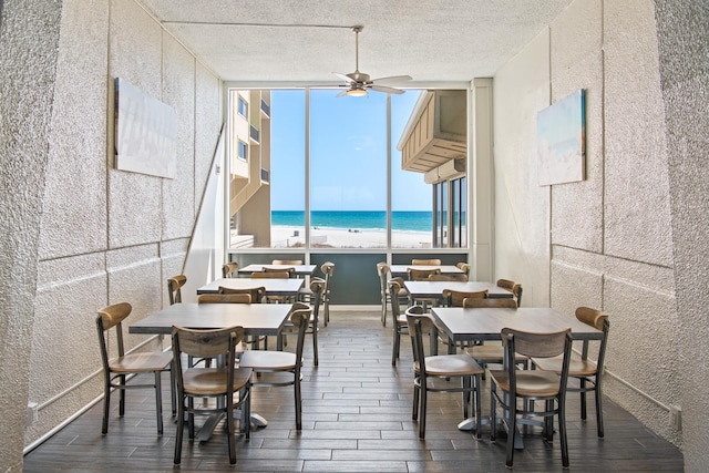 dining area featuring a water view, a textured ceiling, baseboards, ceiling fan, and wood tiled floor