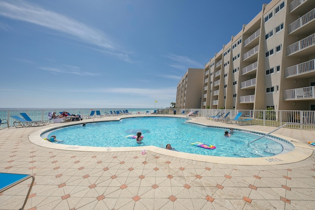 pool with a patio area, a water view, and fence