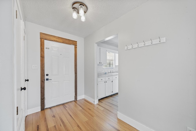 foyer with light wood finished floors, a textured ceiling, and baseboards