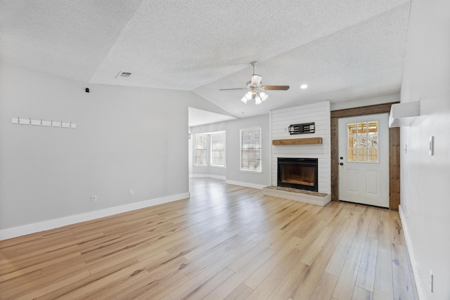 unfurnished living room featuring visible vents, a large fireplace, light wood-style floors, ceiling fan, and vaulted ceiling