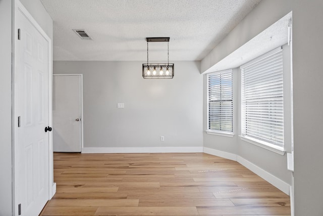 unfurnished dining area featuring light wood-type flooring, baseboards, a textured ceiling, and visible vents