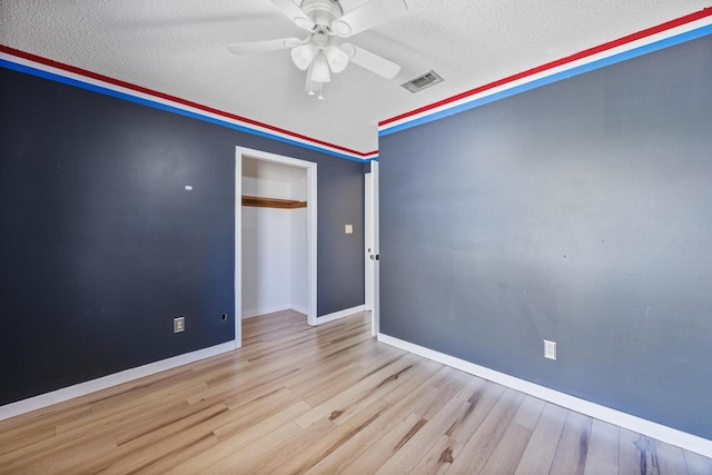 empty room with a ceiling fan, baseboards, wood finished floors, visible vents, and a textured ceiling