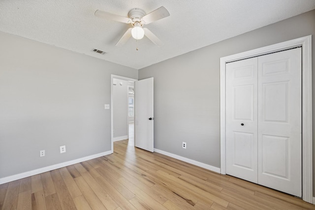 unfurnished bedroom featuring visible vents, baseboards, light wood-style floors, a closet, and a textured ceiling