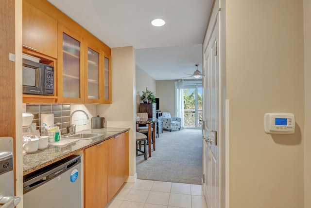 kitchen with light stone counters, a sink, black microwave, stainless steel dishwasher, and light colored carpet