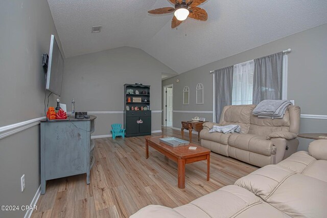 living area with baseboards, light wood finished floors, ceiling fan, vaulted ceiling, and a textured ceiling